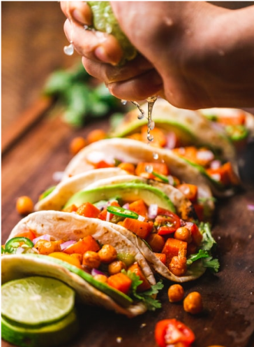 A hand squeezing lime juice onto several tacos. 
